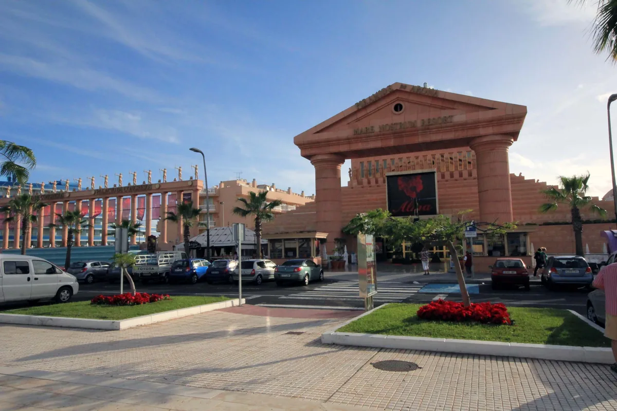 The pink stone entrance gate of the Mare Nostrum Resort, with a pediment on two tall columns, a screen under it and palm trees on the right