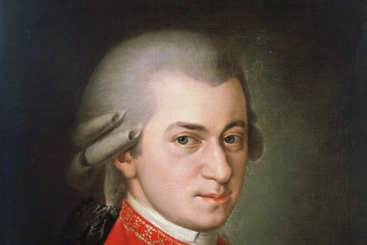 A painted portrait of Wolfgang Amadeus Mozart, with a grey wig and a red coat trimmed with gold